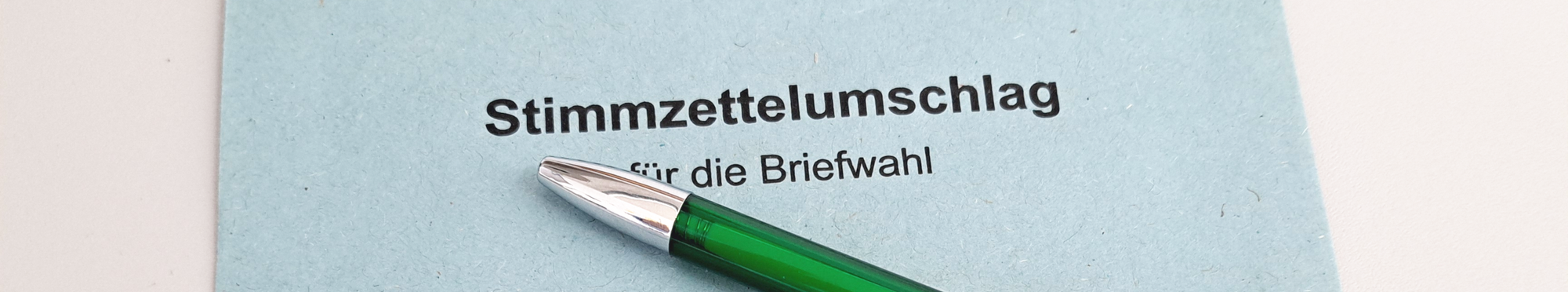 Ein blauer Briefwahlumschlag auf dem ein grüner Kugelschreiber mit dem Logo der Stadt Erftstadt liegt