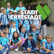 Im Vordergrund steht: "Sommer 2023: Ferienspiele in Erftstadt". Rechts oben ist das Logo der Stadt Erftstadt. Im Hintergrund sitzen und stehen Kinder und Jugendliche zusammen auf dem Boden.
