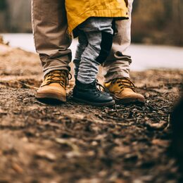 Füße und Waden einer erwachsenen Person und eines Kindes, mit Wanderschuhen im Wald. Froschperspektive