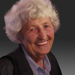 Porträt einer freundlich lächelnden alten Dame mit weißem, gelockten Haar.